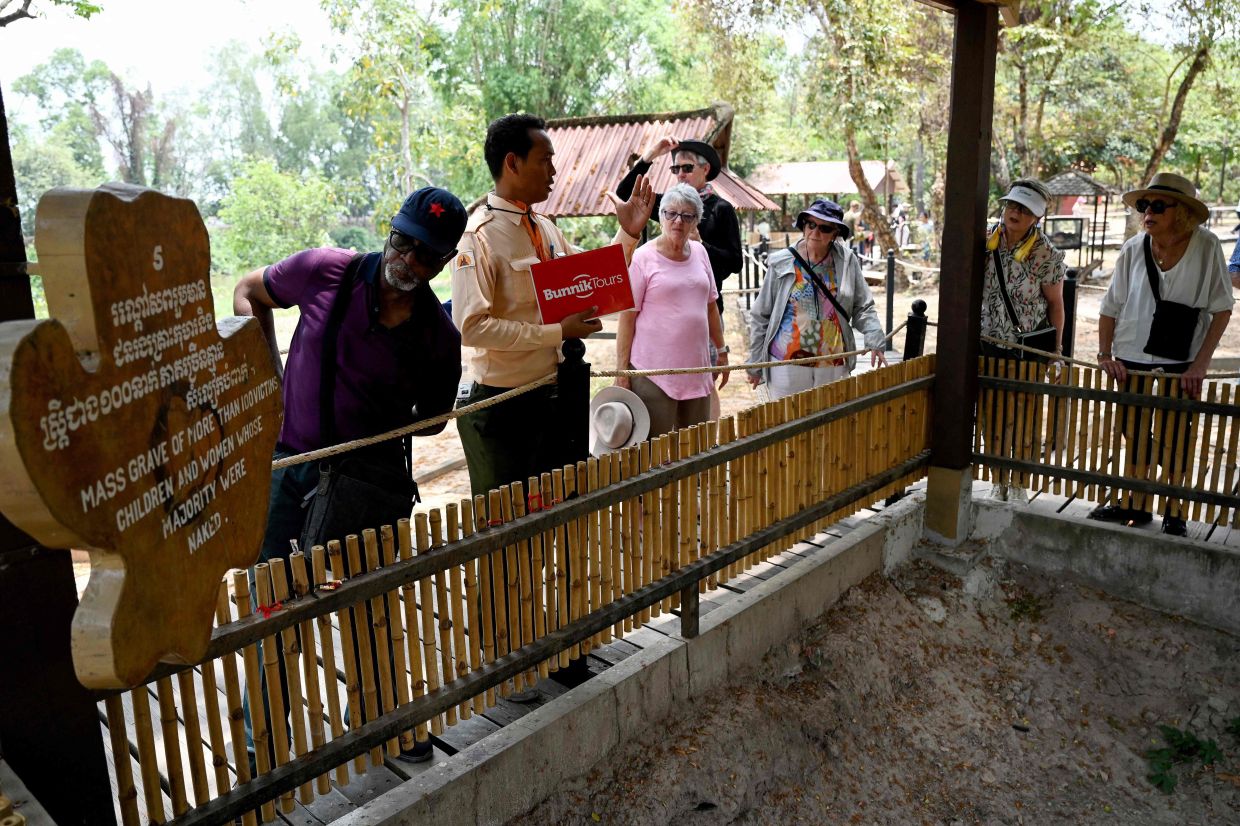 A Cambodian guide (second left) briefing tourists next to a mass grave of victims of the Khmer Rouge regime at the Choeung Ek Killing Fields Memorial in Phnom Penh. - AFP