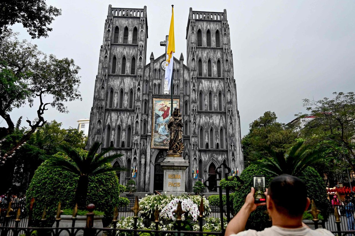 A man takes a photo of St. Joseph Cathedral in Hanoi on Monday, April 21, 2025. Pope Francis died on April 21, 2025 aged 88, a day after making a much hoped-for appearance at Saint Peter's Square on Easter Sunday, the Vatican said in a statement. -- Photo by Nhac NGUYEN / AFP