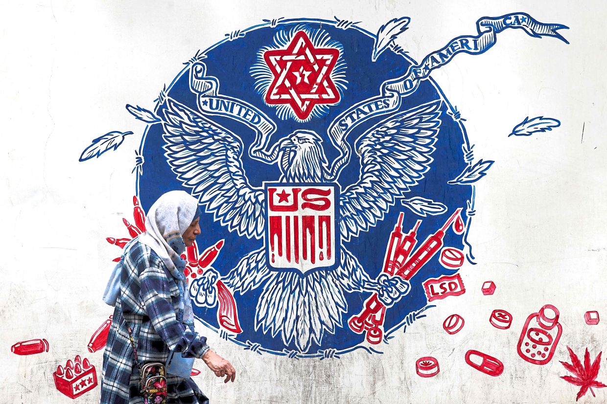 Trust deficit: A woman walking past a mural depicting a mock version of the Great Seal of the United States, with the eagle holding syringes and ammunition cartridges in its talons and a Star of David painted above with other drugs and firearms nearby, painted on the outer walls of the former US embassy in Teheran, Iran. — AFP