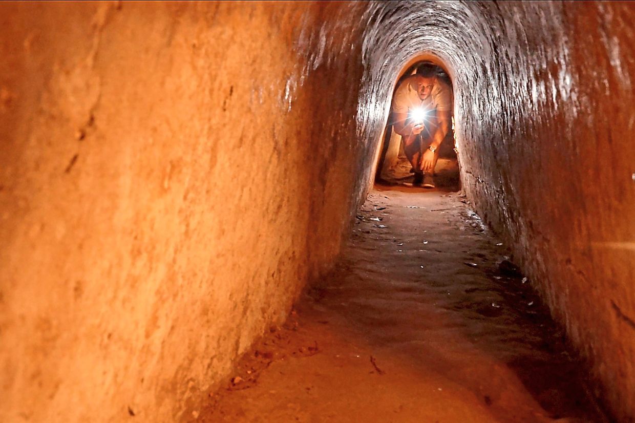 A tourist moving in a narrow tunnel passage in the relic site of Cu Chi tunnels.
