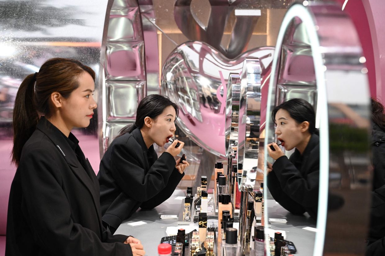 Staff members practice putting on makeup in a pop-up Yves Saint Laurent store in the Wangfujing shopping street in Beijing on Monday, May 5, 2025, the last day of a five-day national May Day holiday. -- Photo by GREG BAKER / AFP