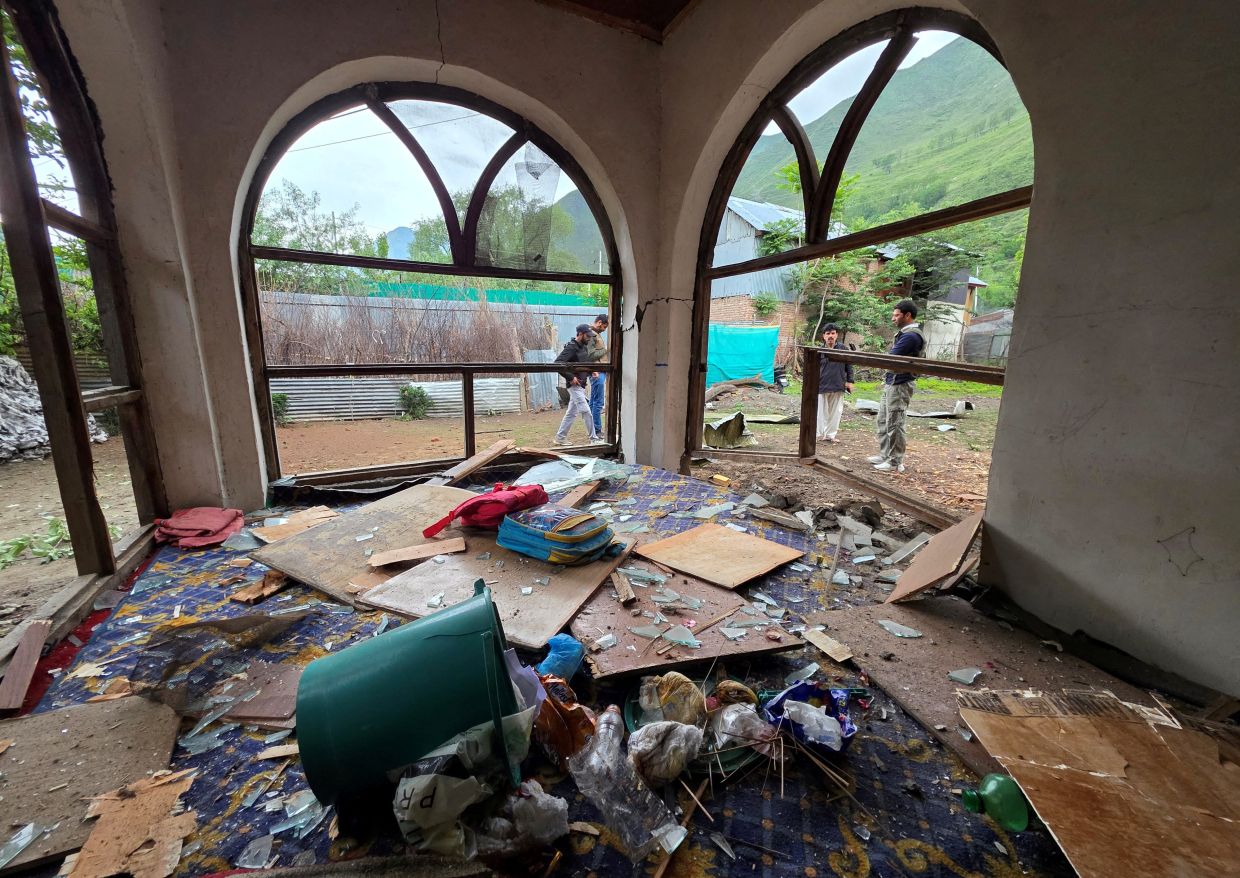 Men are seen through windowpanes of a residential house damaged by a cross-border shelling in Gingal village near the Line of Control between India and Pakistan, in Indian Kashmir's Baramulla district, on May 9, 2025. - Reuters