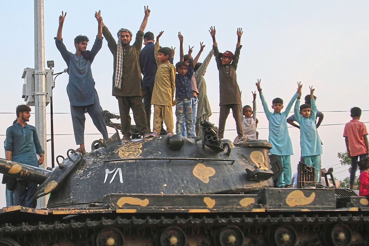 Pakistanis flash victory signs as they celebrate on top of a model of a tank following the ceasefire deal in Multan.-AP