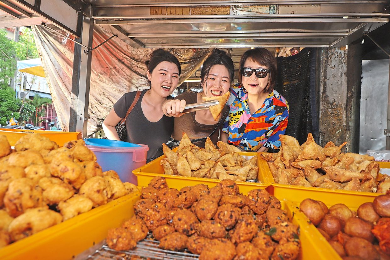 (From left) Postgraduate students Zhang Jing Lun, 32, Xing Zhang, 33, and He Ying Lei, 40, at the Michelin-selected samosa stall in Penang’s Little India. — LIM BENG TATT/The Star