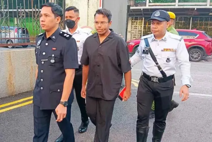 A Singaporean civil servant is escorted by police officers to the Magistrate's Court. Photo: The Star (2025)