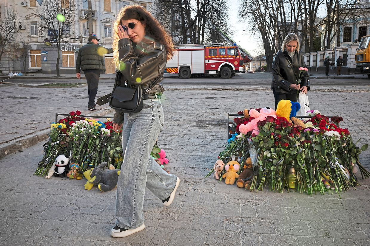 Firefighters battling a blaze after a Russian drone struck a parking lot in Sumy; (above) mourners at an impromptu memorial for Palm Sunday attack victims. — Tyler Hicks/The New York Times