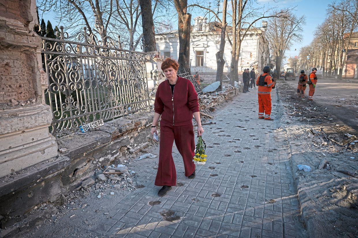 A woman arrives on Monday, April 14, 2025, to lay flowers at an impromptu memorial to those killed in the Palm Sunday missile attack on Sumy, Ukraine. Threats of air attacks repeatedly disrupted the cleanup work at the site of Sunday’s attack, a sprawl of burned cars and splays of brick on the sidewalks. (Tyler Hicks/The New York Times)