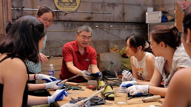 Artisan Nguyen Van Truong (middle) guides a group of tourists on how to make tyre sandals. - VNS
