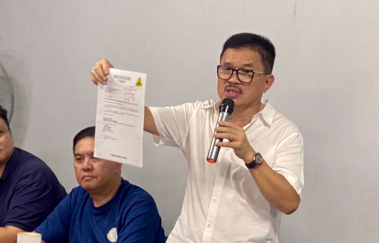 Tan Sri Liew Yun Fah holds up an official land approval document during a dialogue session with residents in Tawau, emphasising the government's commitment to resolving longstanding land issues.