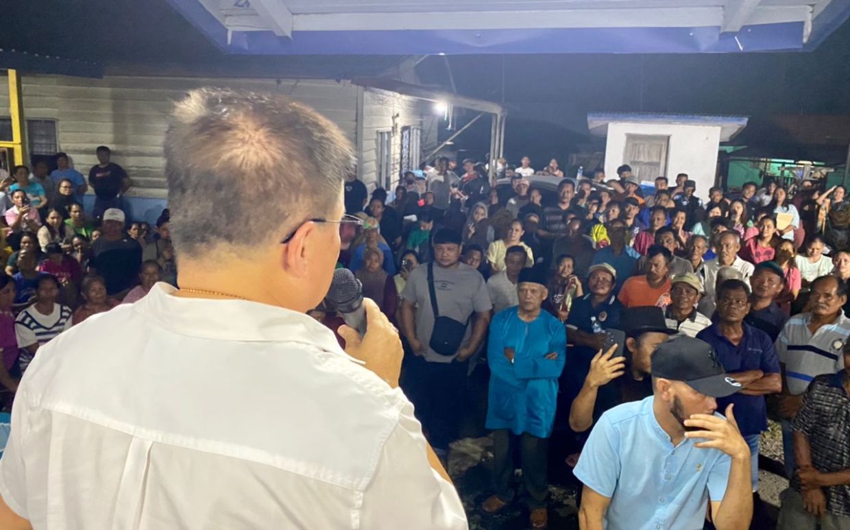 Tan Sri Liew Yun Fah addresses a large crowd of residents at Kampung Sentosa Blok 4 in Tawau, assuring them that the land gazettement process for their settlement is progressing.