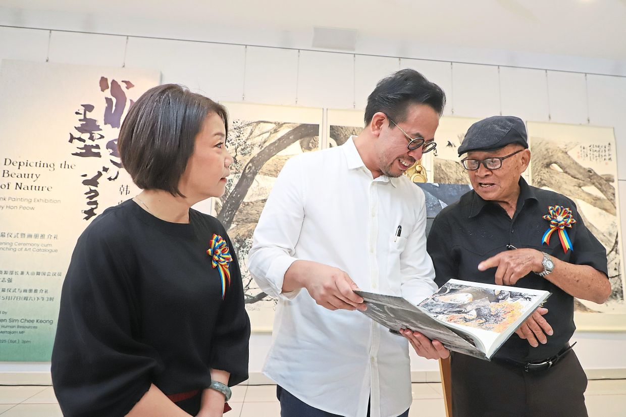 Hon Peow (right) showing the exhibition catalogue to Sim while curator Tan Chin Joo looks on.
