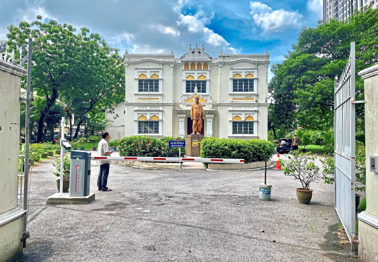 A man at the entrance of Vivekananda Ashram looking at the colonial facade of the building and the statue of Swami Vivekananda.