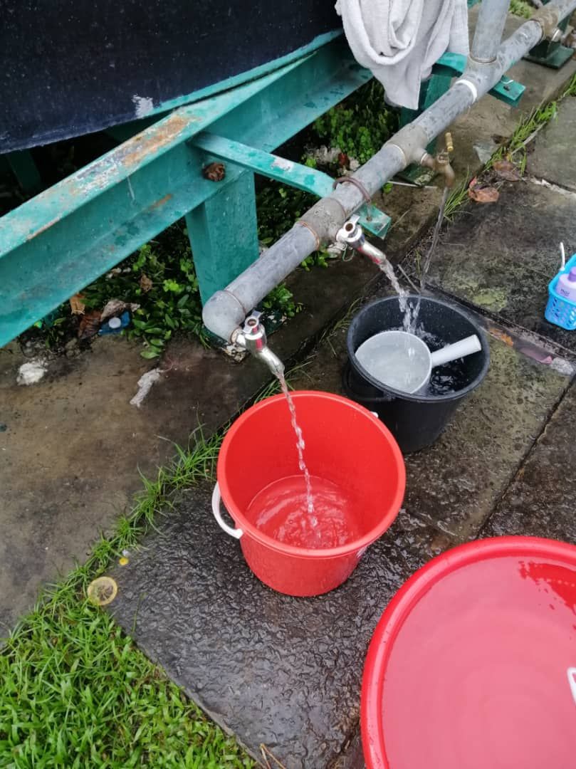 Students fill buckets from a communal outdoor pipe system at Universiti Malaysia Sabah (UMS) amid ongoing water supply disruptions.