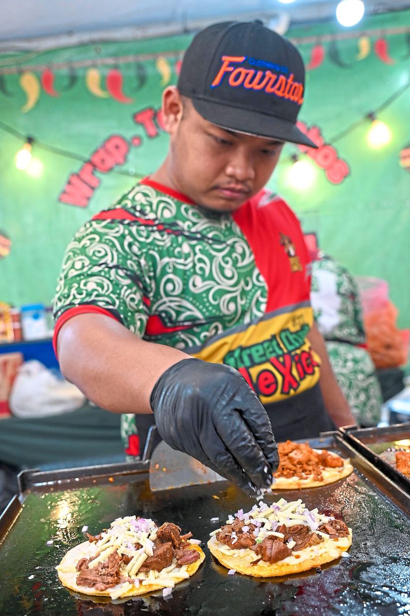 Worker at a stall selling Mexican street food preparing the Mozarella Birria Tacos.