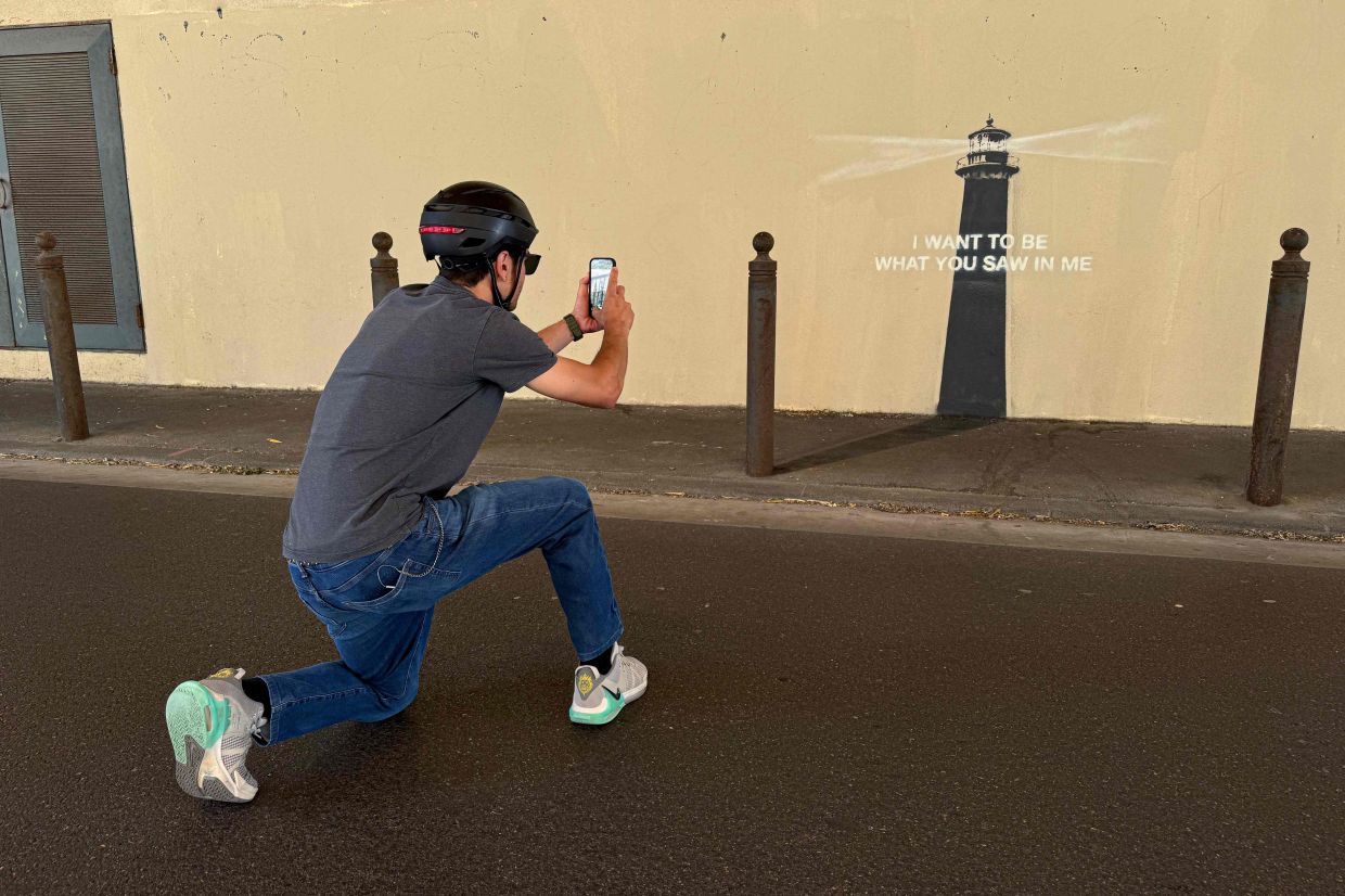 A pedestrian takes a photograph of a newly released artwork by street artist Banksy on the facade of a building in Marseille, southeastern France, on May 30, 2025. — Photo: Viken KANTARCI/AFP