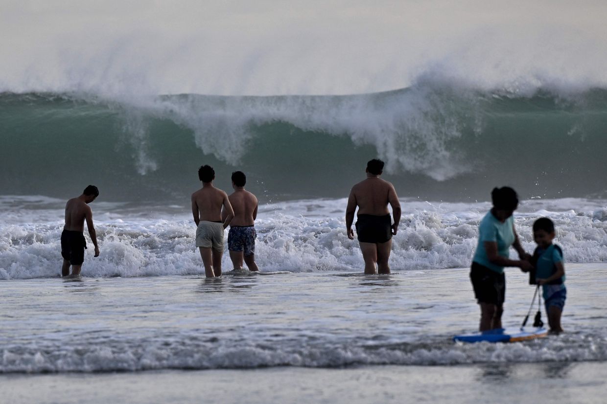 Beachgoers look on as a large wave crests at Kuta beach near Denpasar, Indonesia's Bali island on Saturday, May 31, 2025. -- Photo by SONNY TUMBELAKA / AFP