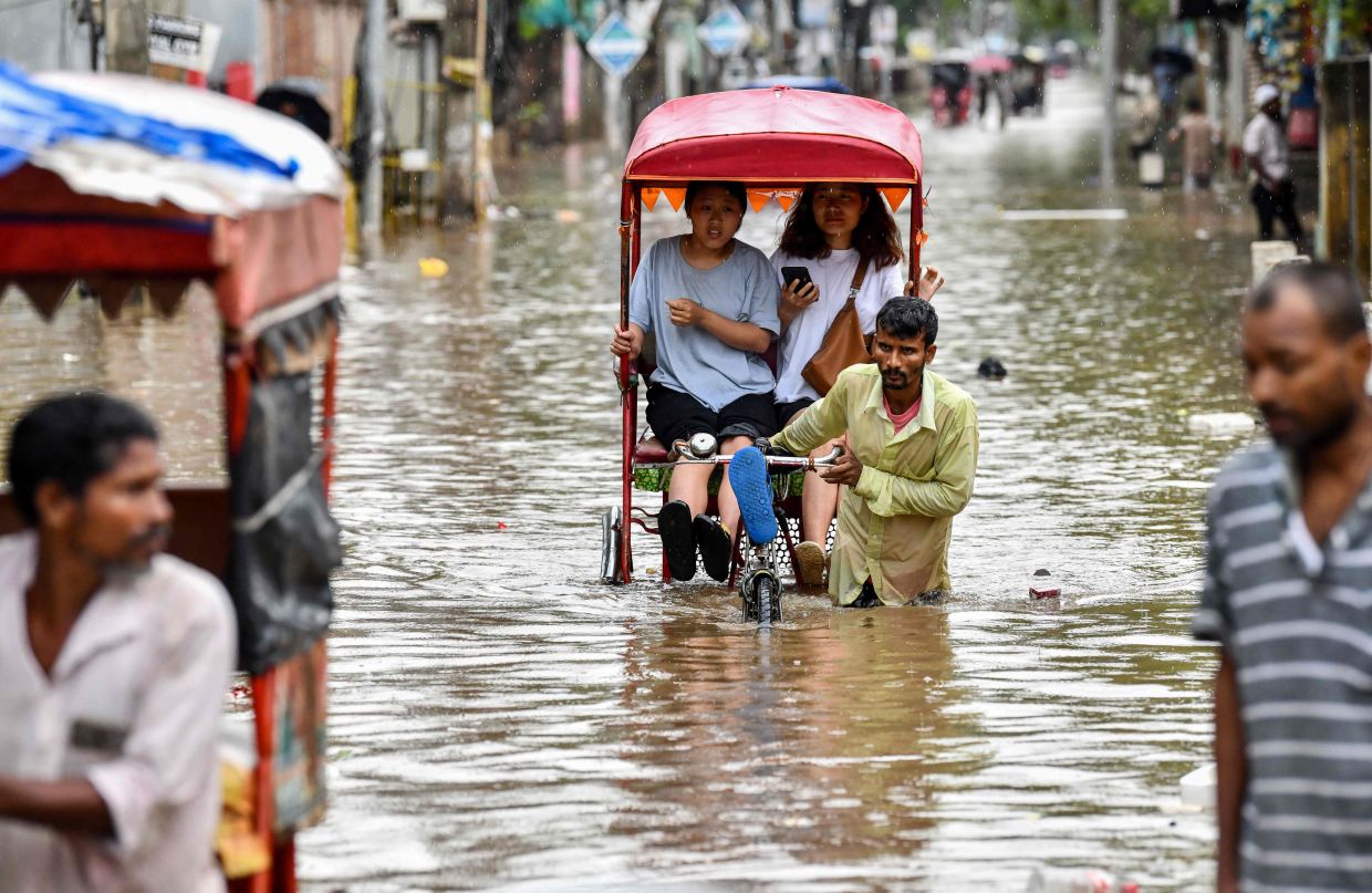 Women commute in cycle rickshaws through a flooded street after heavy rains in Guwahati, in India's Assam state. Torrential monsoon rains in India's northeast triggered landslides and floods that swept away and killed at least five people in Assam, disaster officials said on May 31. -- Photo by Biju BORO / AFP
