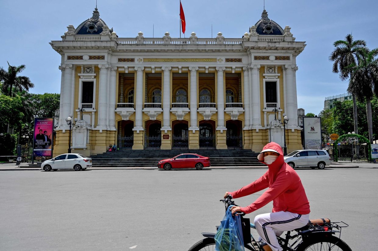 A woman wearing a long-sleeve top and a sun visor to protect against UV rays rides a bicycle past the Hanoi Opera House on a hot day in Hanoi on Monday, June 2, 2025. -- Photo by Nhac NGUYEN / AFP
