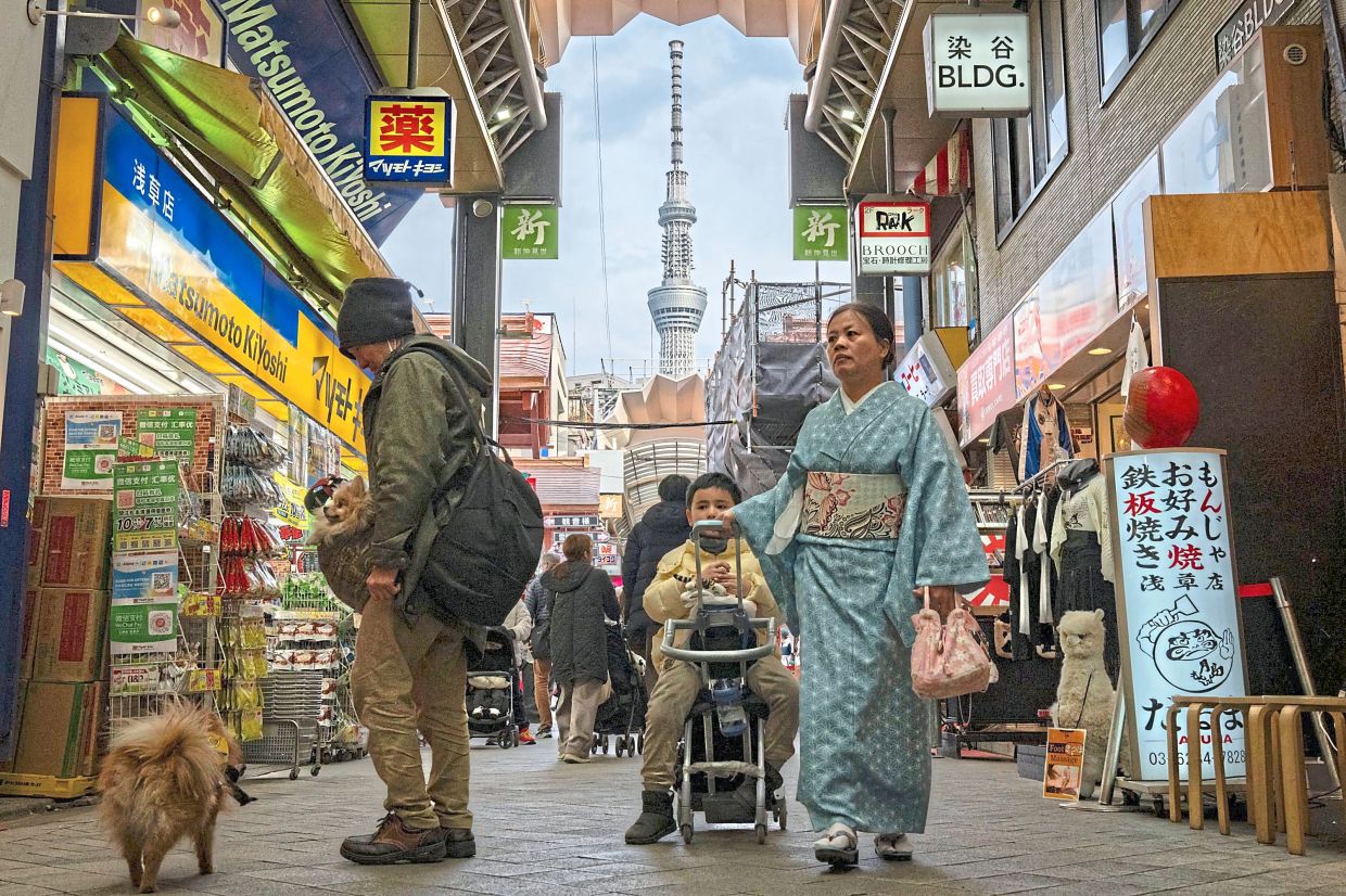 Business as usual: This file photo taken on Feb 21 shows people walking past shops in the Asakusa area as the 634m-high Tokyo Skytree is pictured in the distance in the Japanese capital. — AFP