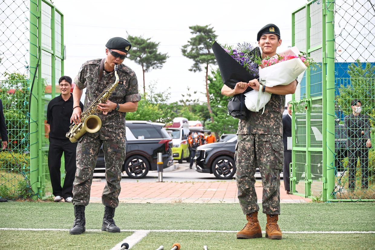 Centre of attention: RM playing a saxophone and V holding bouquets as they arrive for an event after being discharged from mandatory military service, in Chuncheon. — Reuters