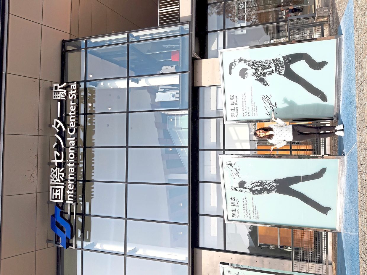 The writer standing between posters of Yuzuru Hanyu, Sendai’s two-time Olympic champion in figure skating.