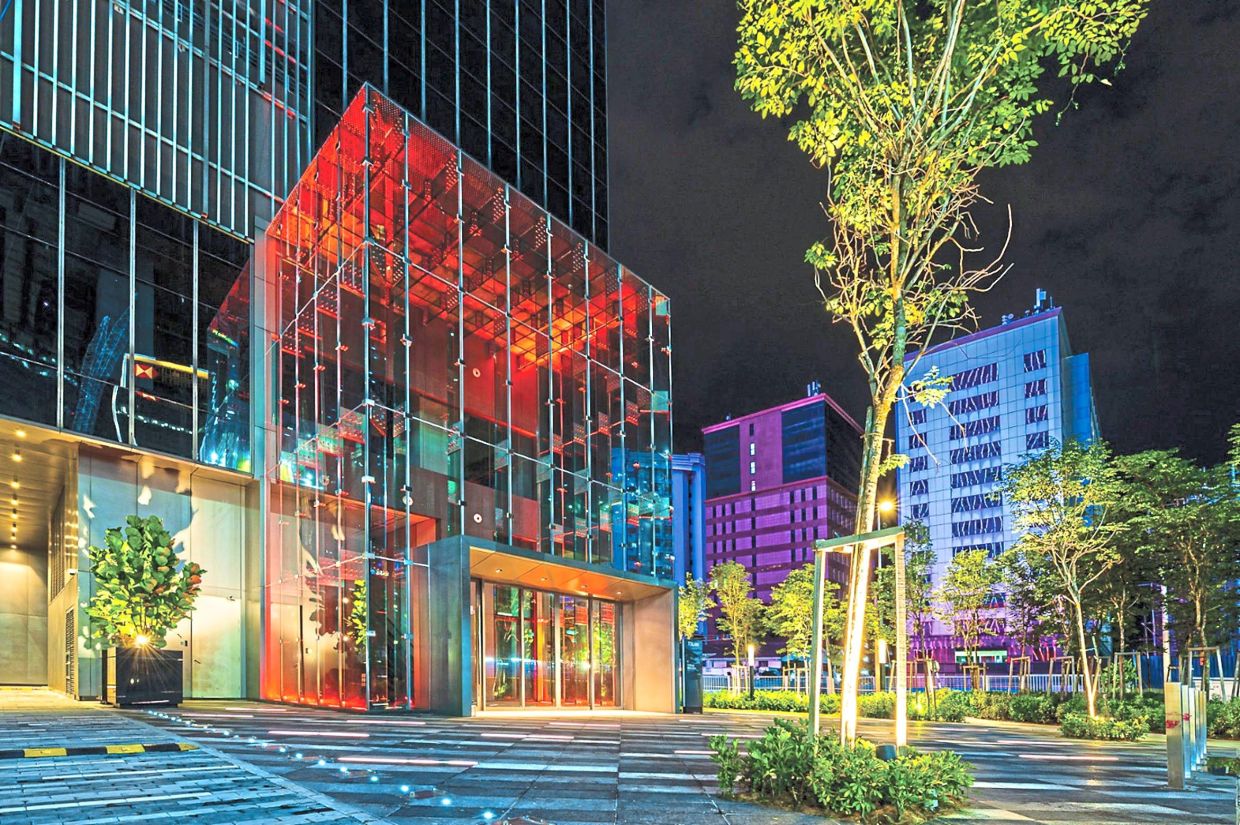 The glass cube entrance and landscape illuminated at night.