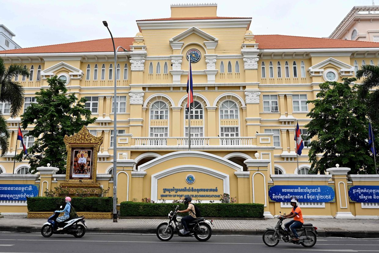 Motorists ride along a street in front of Cambodia's Ministry of Post and Telecommunications in Phnom Penh on June 13, 2025. Cambodia ordered its troops to stay on -- full alert -- on Friday, June 13 in its ongoing border spat with Thailand, as it ordered television stations and cinemas to stop showing Thai dramas. -- Photo by TANG CHHIN Sothy / AFP