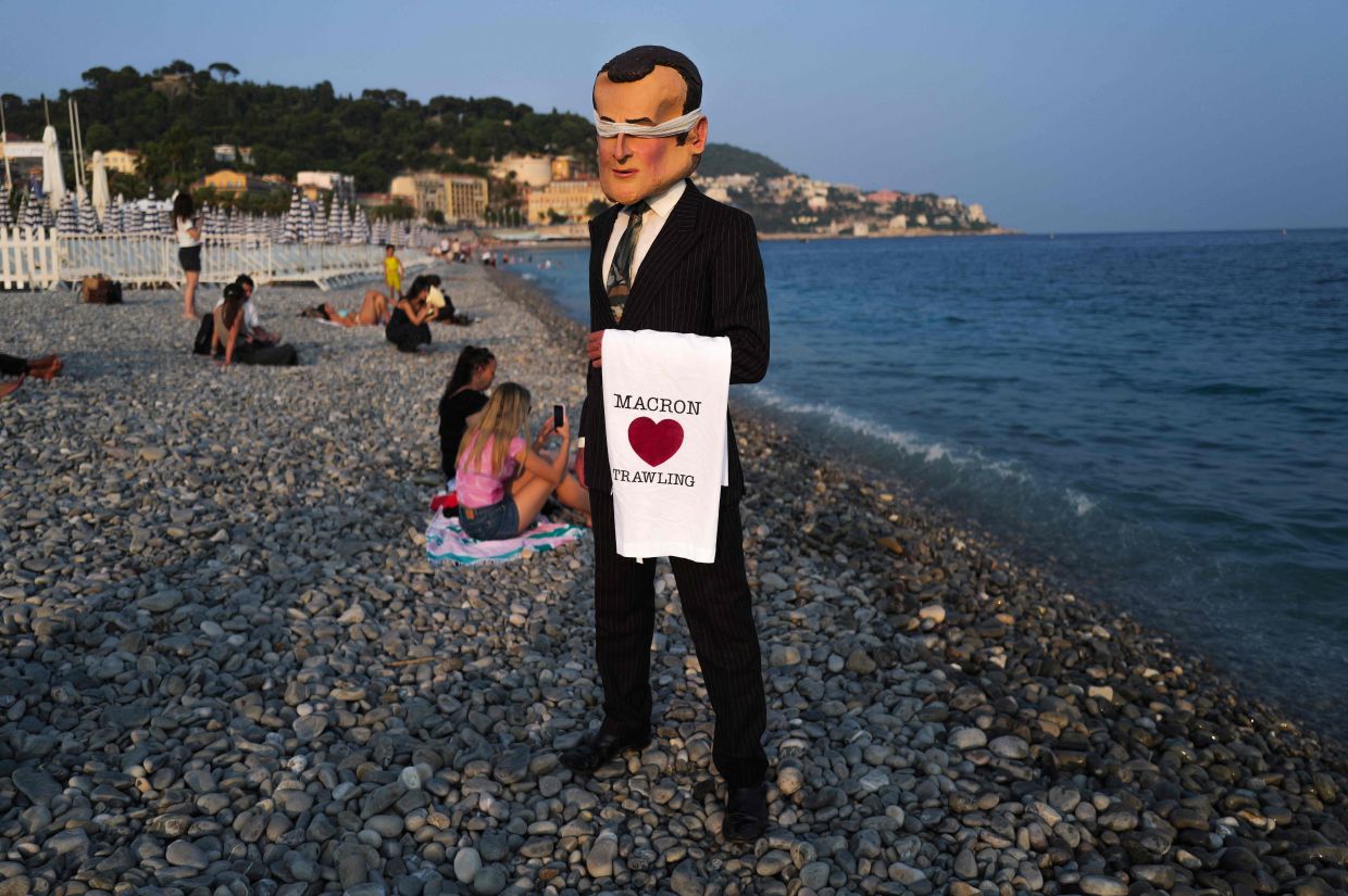 A member of Ocean Rebellion dressed in a costume of France's President Emmanuel Macron with banded eyes stands on the beach along the Promenade des Anglais on the sidelines of the third United Nations Ocean Conference (UNOC3), in the French Riviera city of Nice, on June 10, 2025. -- Photo by Valery HACHE / AFP