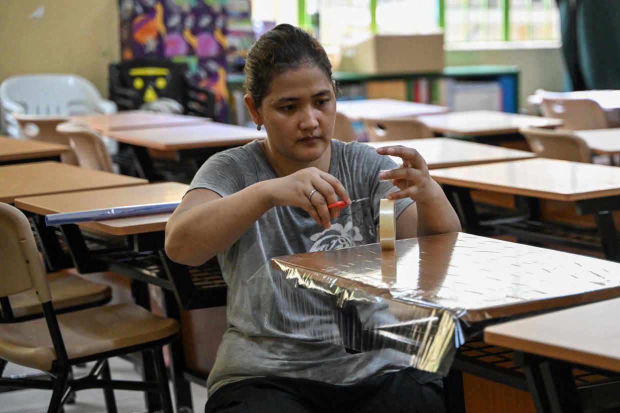 A parent covers a desk with a plastic as she helps with the cleaning of a classroom at an elementary school in Manila ahead of the opening of classes on Monday, June 16, 2025. -- Photo by Jam STA ROSA / AFP