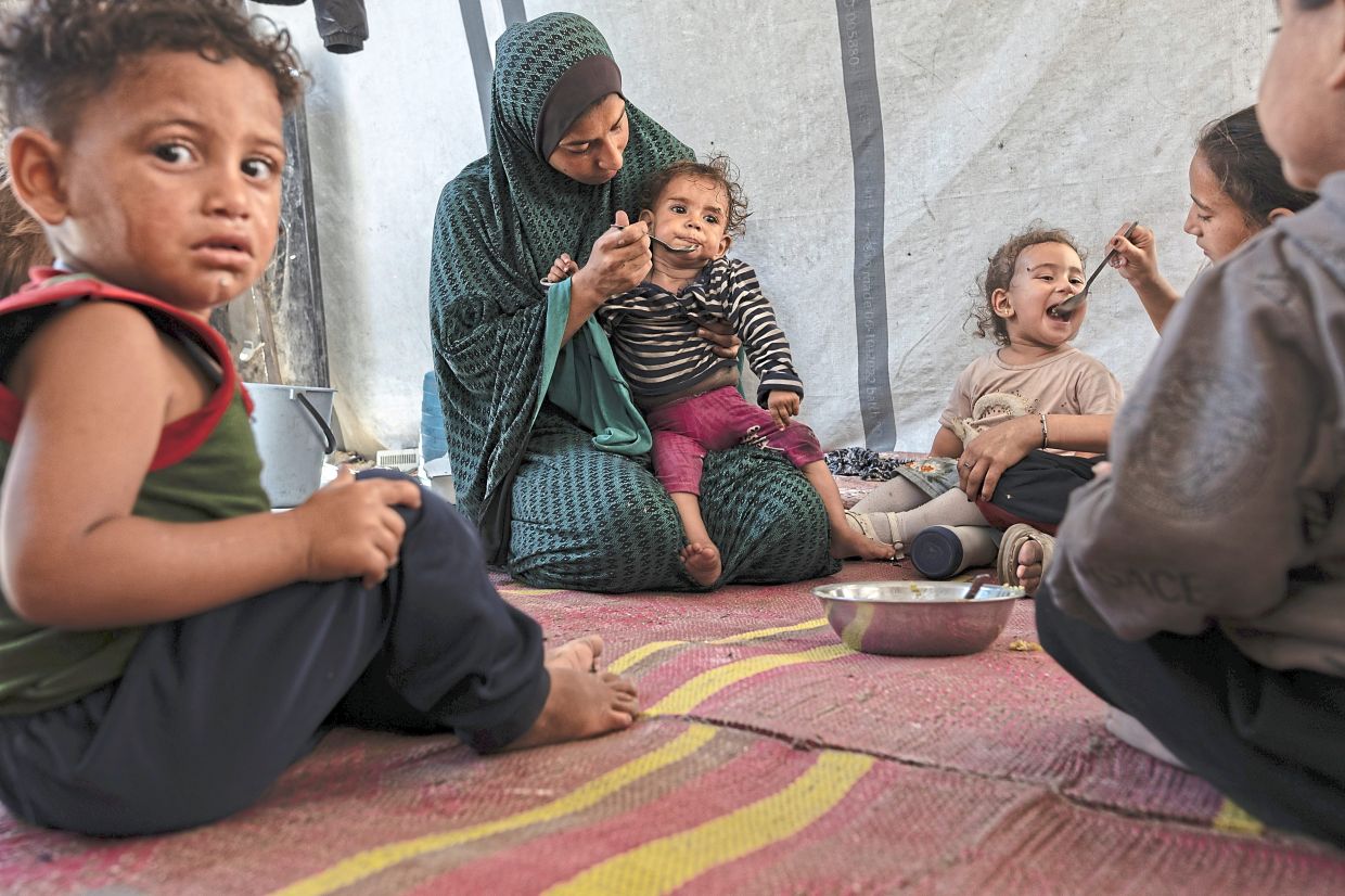 A Palestinian family displaced from Beit Hanoun share a meal of simple bulgur, with bread and basic food supplies scarce, at a UNRWA school in Gaza City in May. — Saher Alghorra/The New York Times