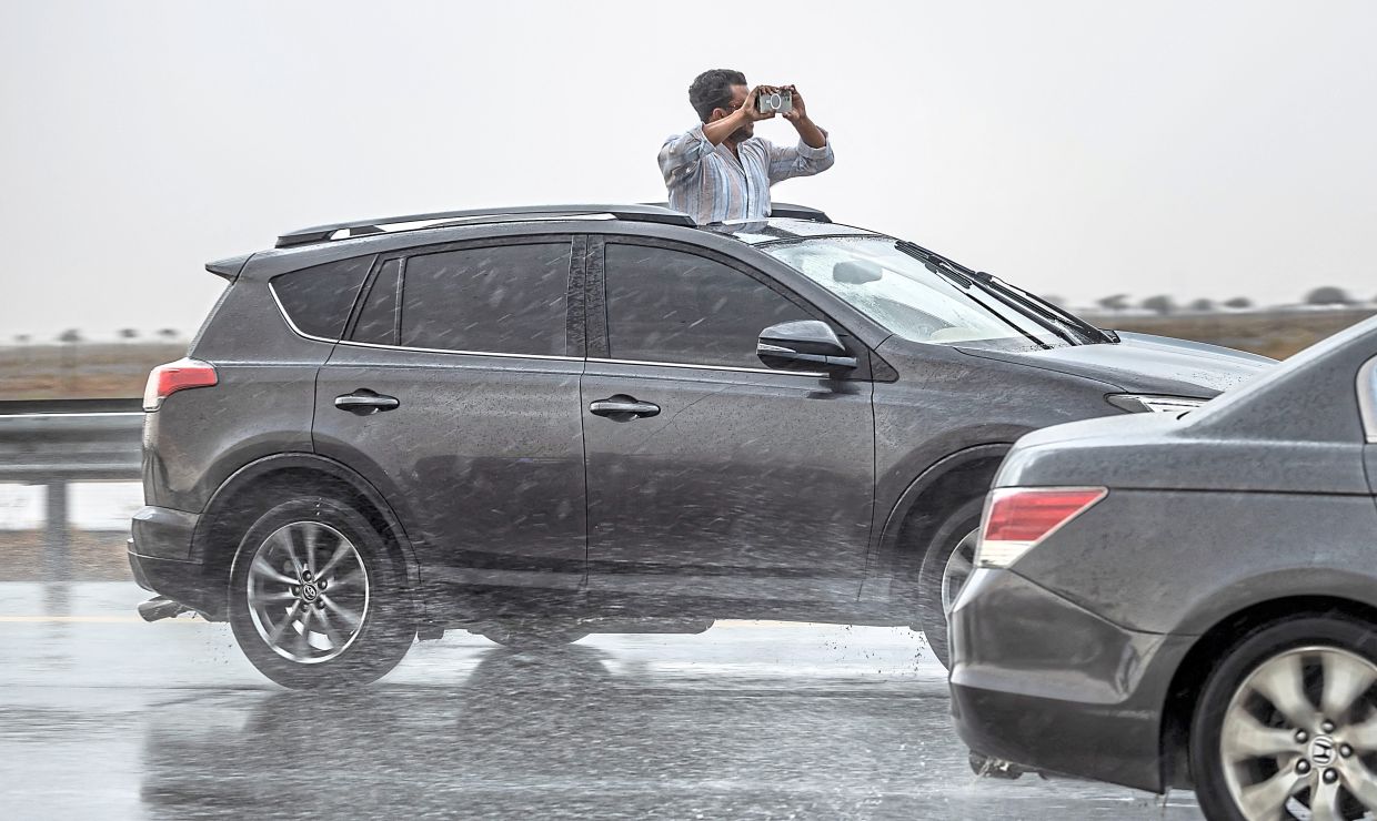 A man taking a selfie through the sunroof of a car during a downpour in Sharjah.