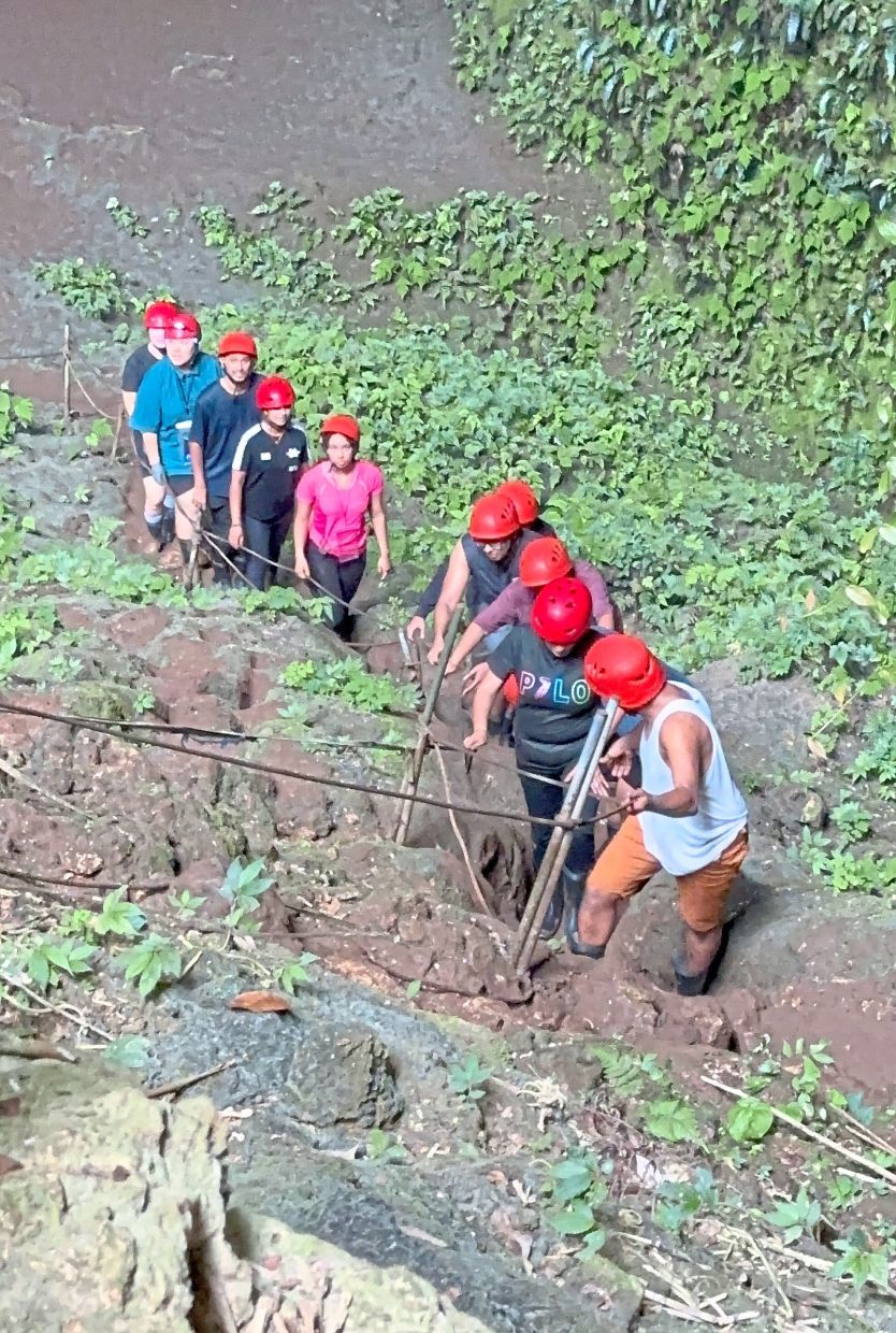 Cavers walking a steep slope to enter the earth’s belly, secured only by thick ropes and local guides.