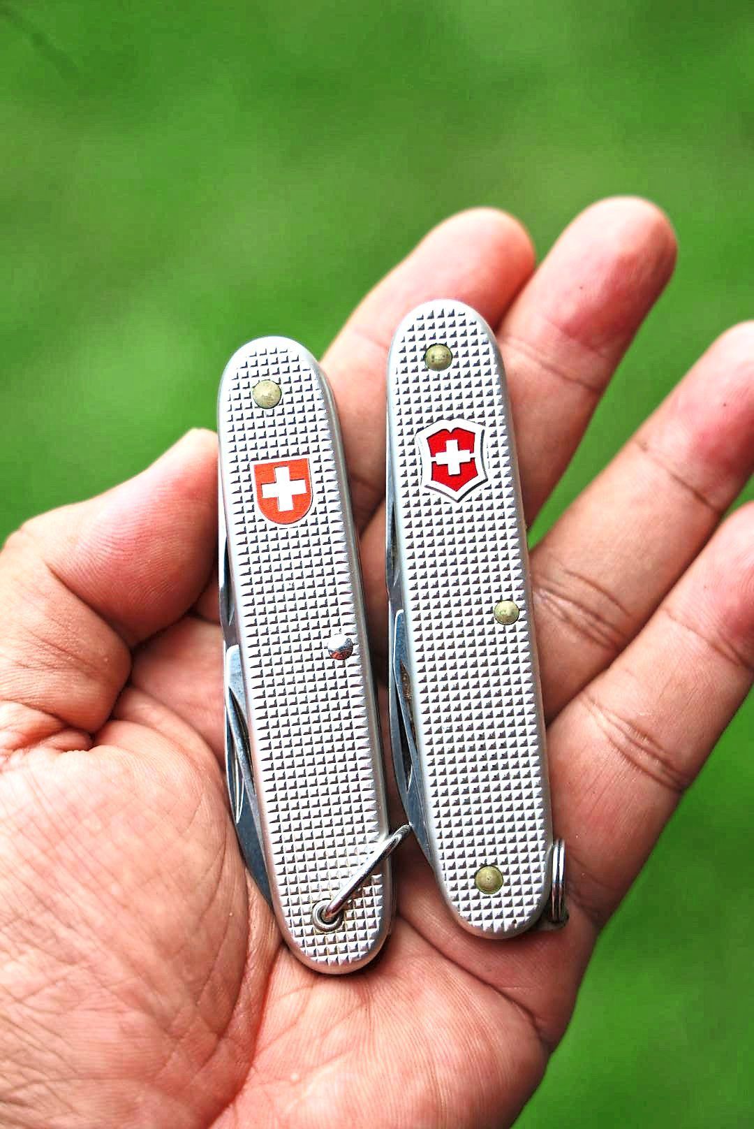 A pair of aluminium-handled Swiss Army Knives made by two companies from Switzerland.