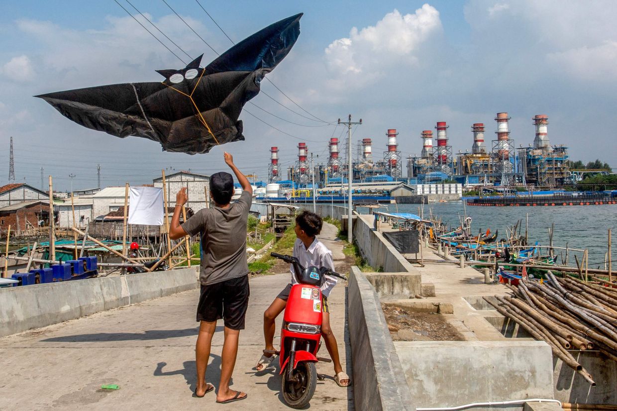Children flying a kite as they play along a seawall built to prevent seawater from entering residential areas, in the coastal village of Tambaklorok, in Semarang, Central Java, Indonesia on June 17, 2025. - AFP