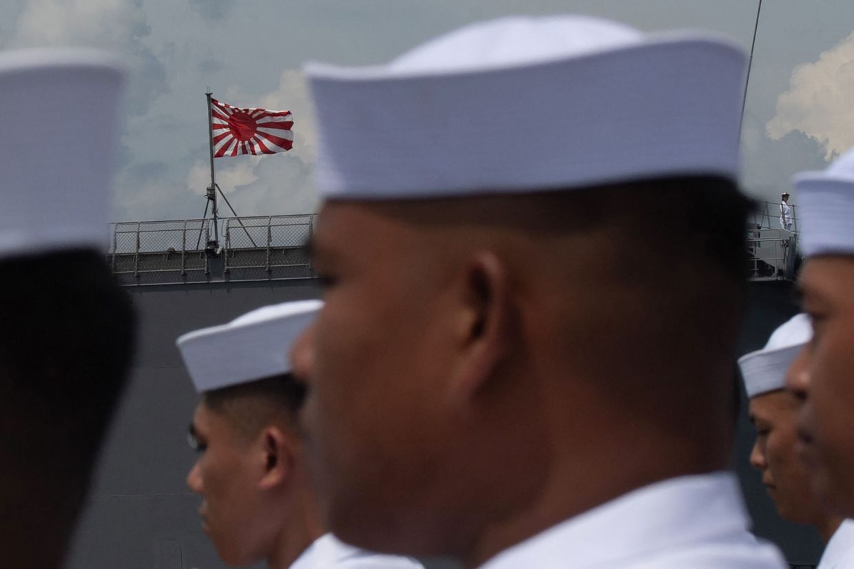 Philippine Navy sailors stand in formation as the Japan Maritime Self-Defense Force ensign on board the JS Ise, a Hyuga-class helicopter destroyer, is seen during a welcoming ceremony at the international port in Manila on Saturday, June 21, 2025. The Ise and Suzunami are on a three-day port call in the Philippine capital. -- Photo by Ted ALJIBE / AFP