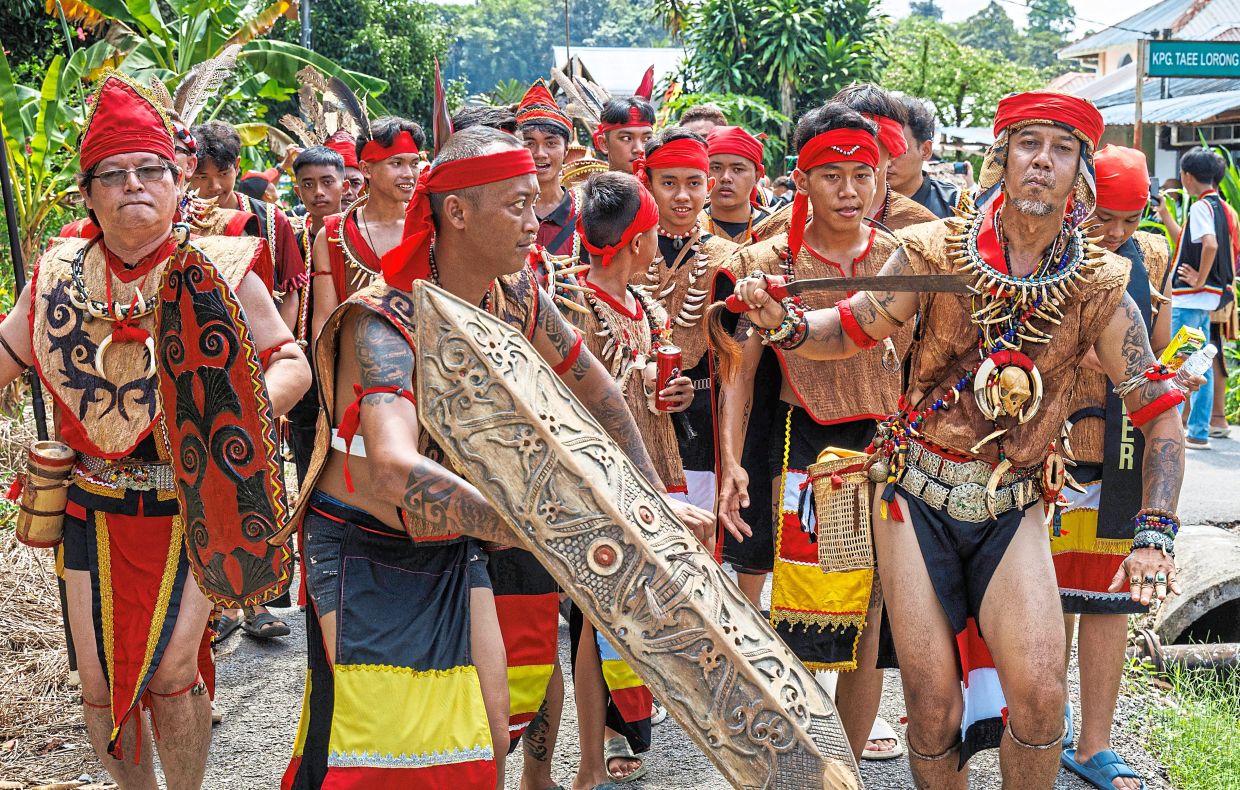 Participants in warrior regalia walking along the parade route through Kampung Taee.
