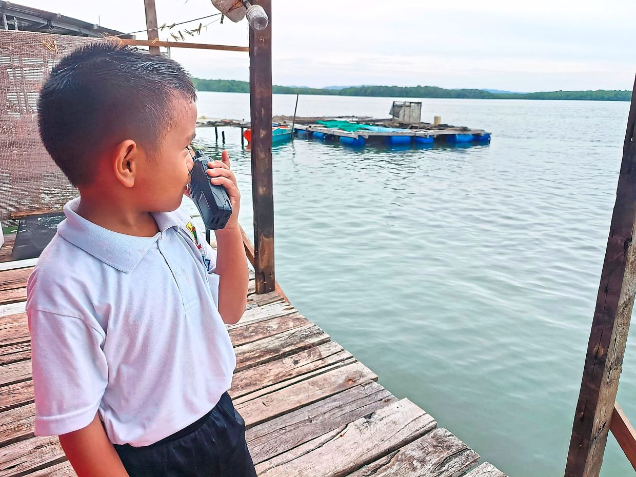 With no mobile coverage on the island, a young boy uses a walkie-talkie to inform his mother that he has reached home after school — one of the few ways villagers in Kampung Keniogan stay connected during the ongoing communication blackout.
