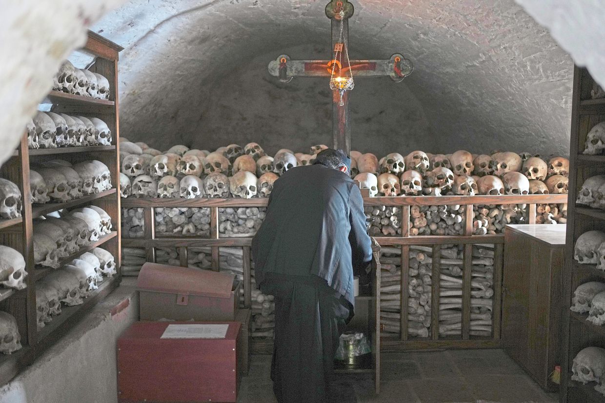Father Serafeim lighting a candle inside an ossuary where the shelves are full of the skulls of the deceased monks of the Simonopetra. — AP