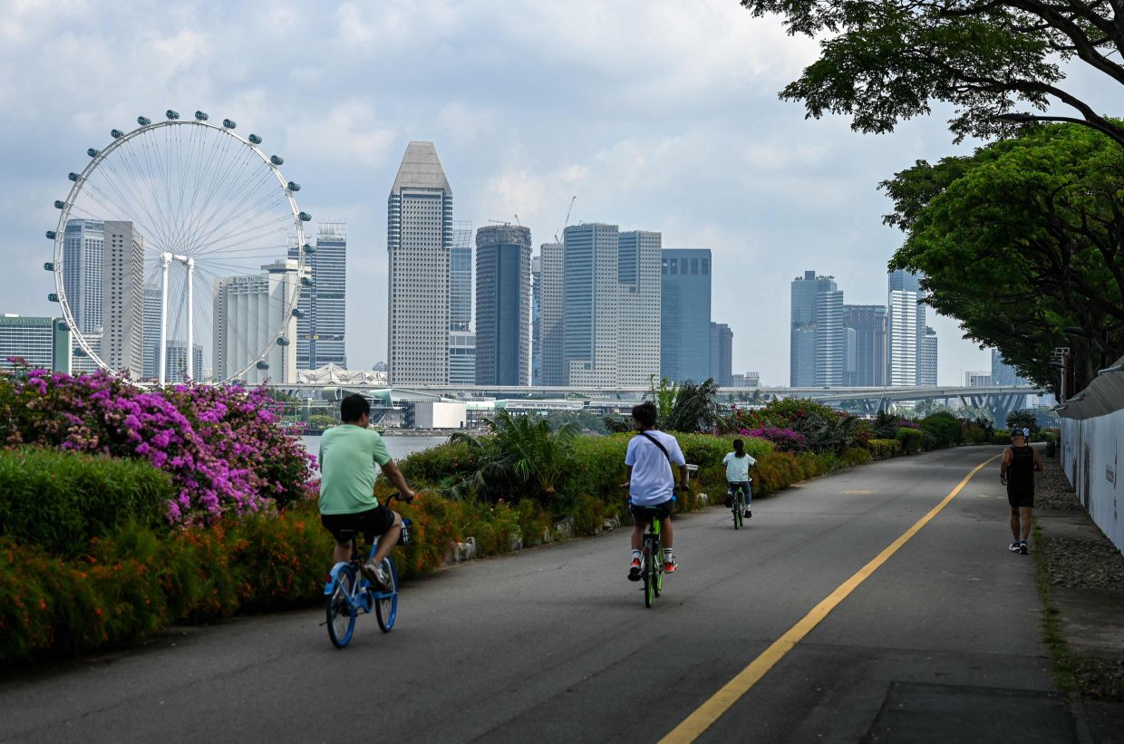 People cycle along a track backdropped with the city skyline in Singapore on June 27, 2025. (Photo by Roslan RAHMAN / AFP)
