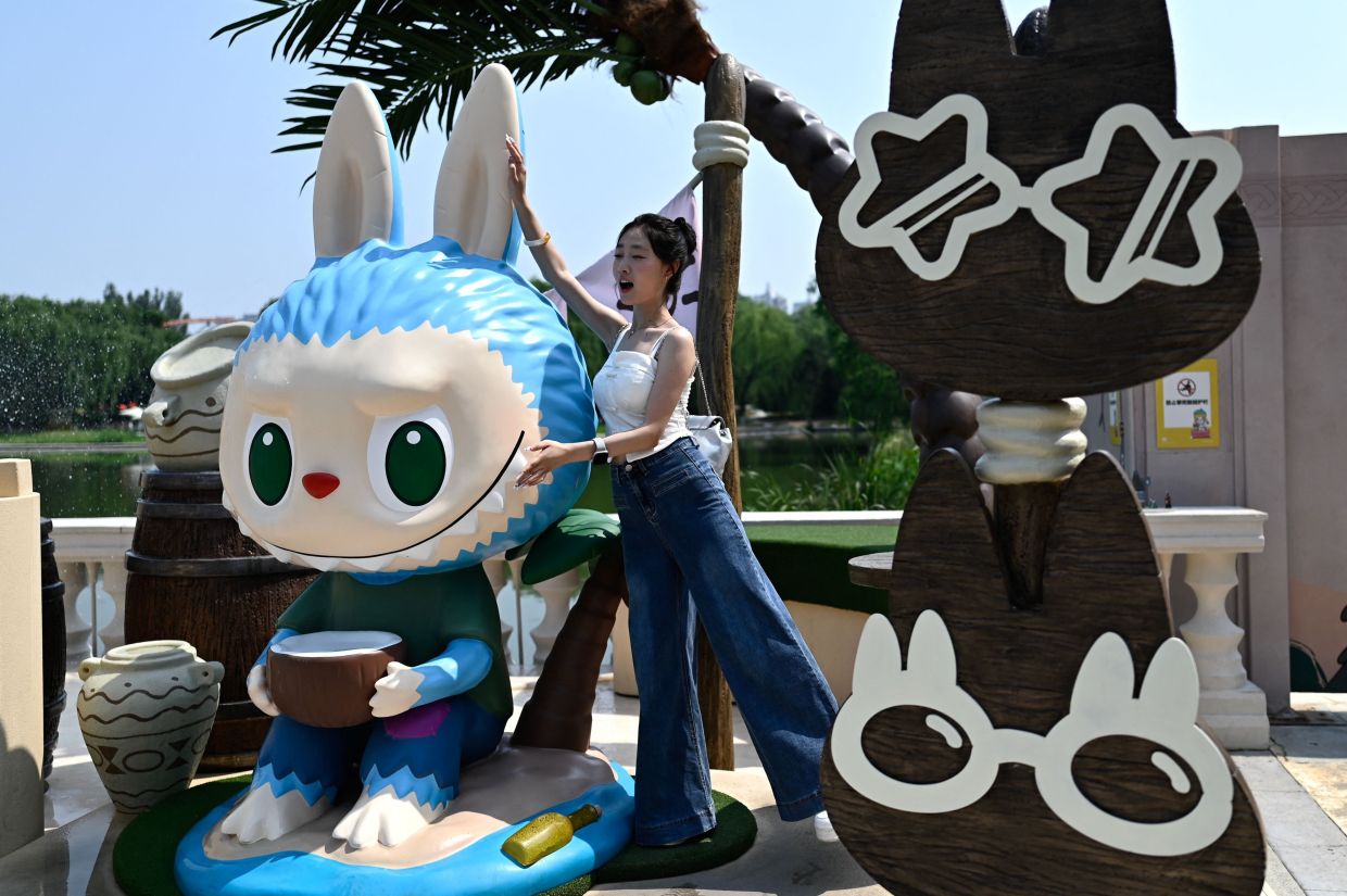 This picture taken on June 18, 2025 shows a woman posing for a picture next to the character Labubu as she visits Pop Marts theme park Pop Land in Beijing. Small, fuzzy and baring sharp teeth, Chinese toymaker Pop Mart's Labubu monster dolls have taken over the world, drawing excited crowds at international stores and adorning the handbags of celebrities such as Rihanna and Cher. (Photo by Pedro PARDO / AFP)