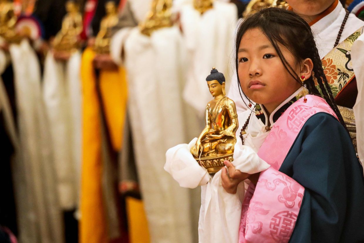 A Buddhist devotee holds a golden Buddha figurine as she waits for the arrival of Tibetan spiritual leader the Dalai Lama, before the start of a Long Life Prayer offering ceremony at the Main Tibetan Temple in McLeod Ganj, near Dharamsala on Monday, June 30, 2025. -- Photo by Sanjay BAID / AFP