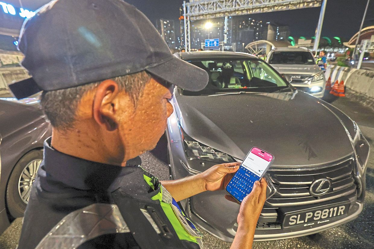 Strict measures: Mohd Alif Rahizad from JPJ checking Singaporean vehicle registration numbers using the ‘VEP Status’ application during the special operation to enforce the VEP, which is effective from yesterday, at Jalan Lingkaran Dalam. — Bernama