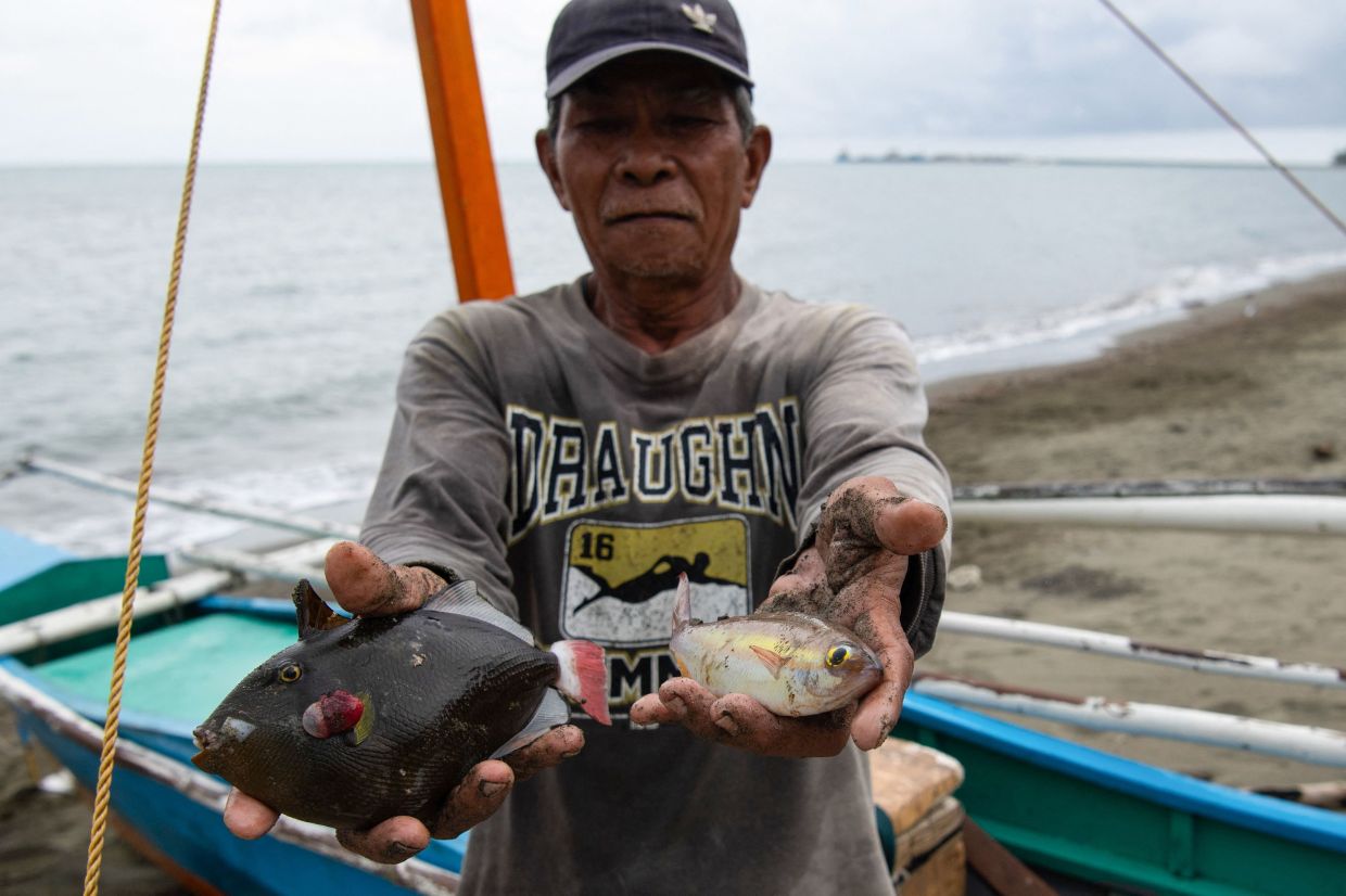 A fisherman showing two fish, his catch of the day, near the pier at the village of Maasin, in Brooke's Point, Palawan province. - AFP