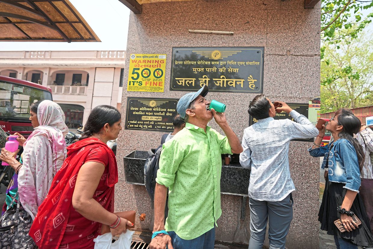 Hydration station: People drinking water at a distribution centre at a bus stop in Ahmedabad. — AP