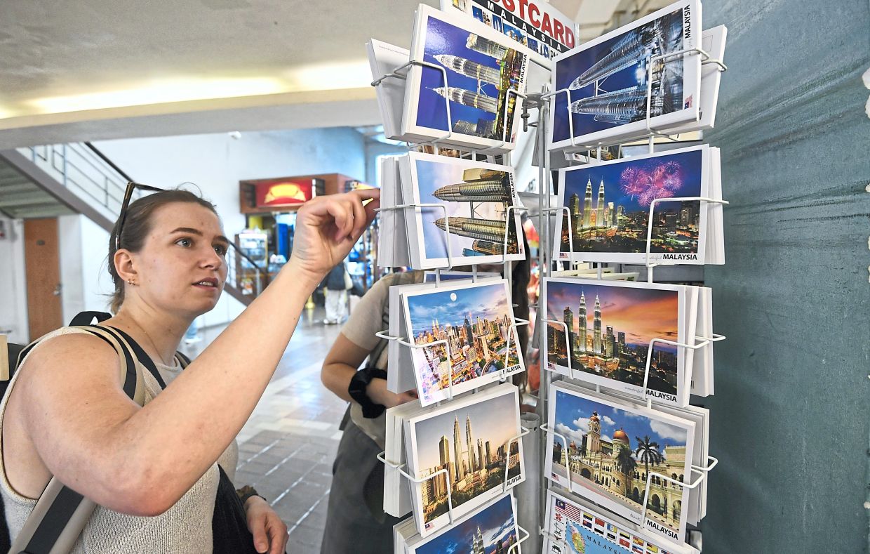 Ahead of Visit Malaysia 2026, tourists select postcards of iconic Kuala Lumpur landmark.