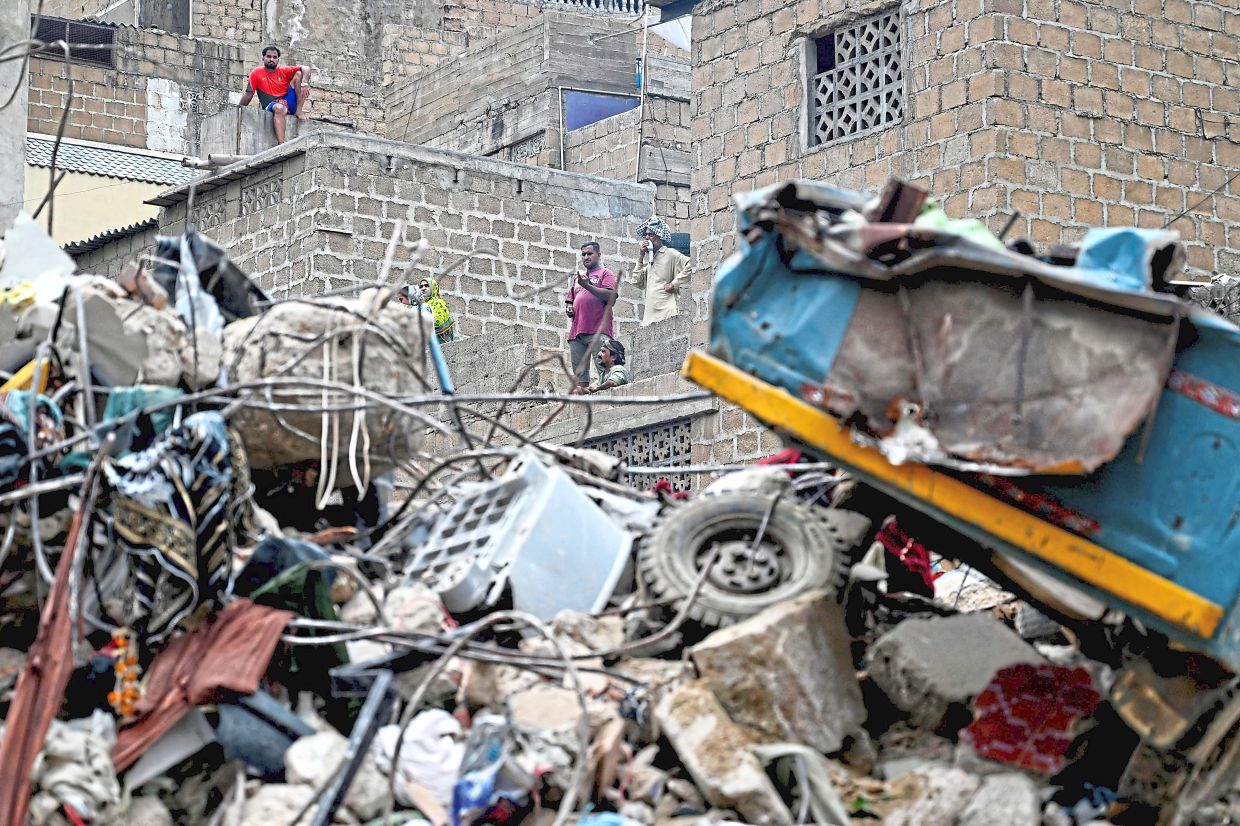In shambles: Residents looking at the debris of a collapsed building from their homes in Karachi. — AFP 