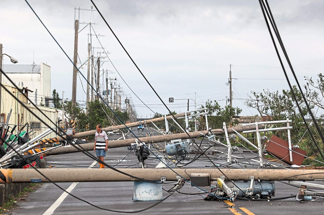 Safety hazard: A man walking among utility poles knocked down by Typhoon Danas in Tainan. — AFP