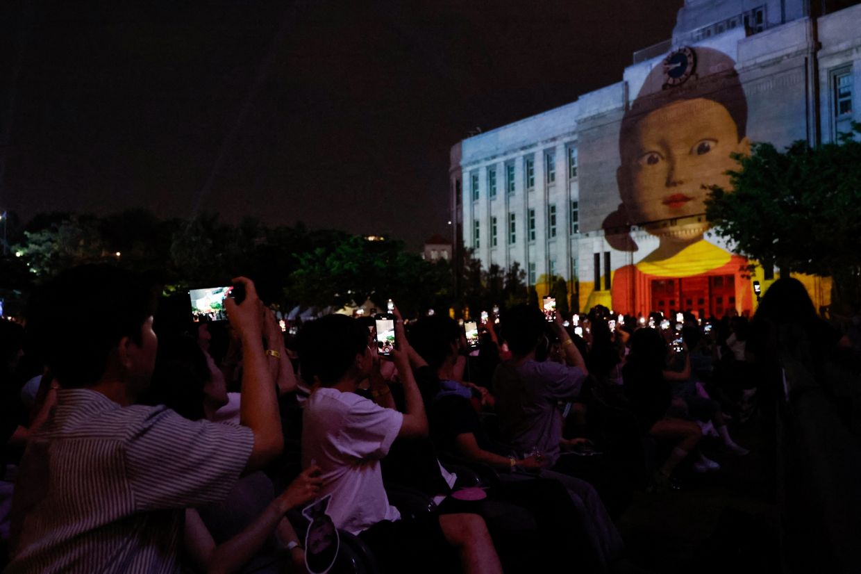 People use their phones as they watch a projection of the killer doll Young-hee from 'Squid Game', before a fan event with cast to celebrate the release of the third season of Netflix's hit series, in Seoul, South Korea, June 28, 2025. Photo: Reuters