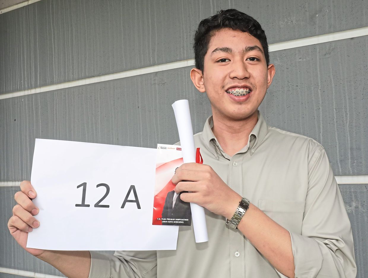 (Front row, from fourth left) Azilawati and Preakas along with students, parents and teachers holding a mock cheque reflecting the total amount the top-performing SPM students received. — Photos: SAMUEL ONG/The Star Muhammad proudly shows his certificate and award.