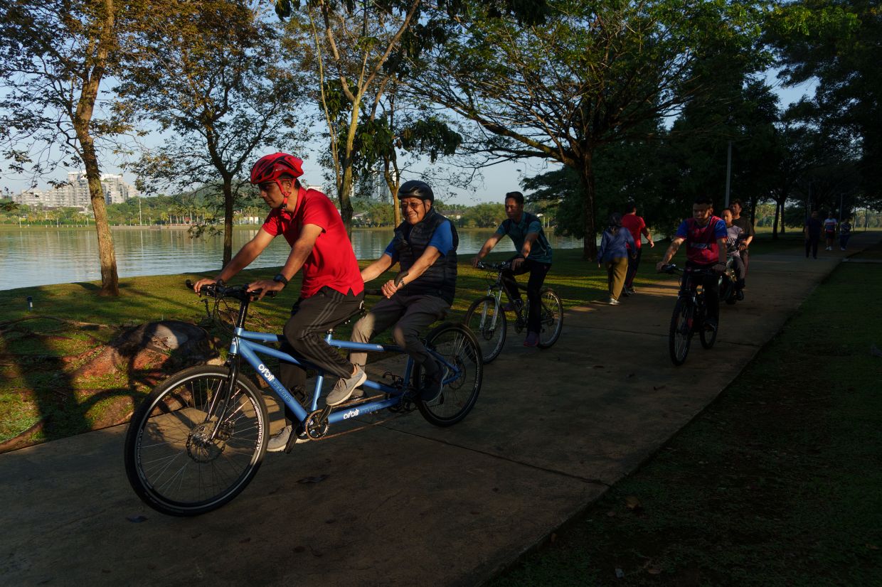 Dr Mahathir, in blue, riding on a tandem bike in Putrajaya. — Chang W. Lee/The New York Times